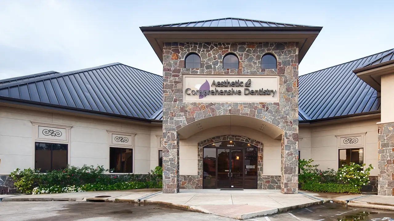 The practice's stone-fronted building at 13810 John Audubon Parkway, Webster, with the Aesthetic & Comprehensive Dentistry sign above the entrance.