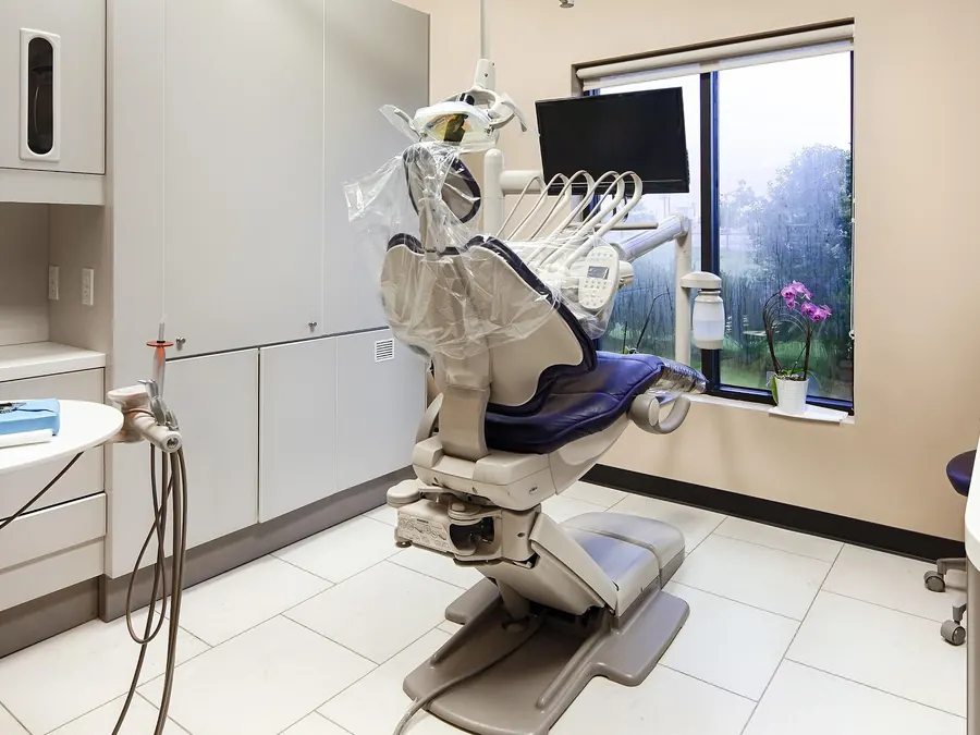 A treatment room with a dental chair, overhead monitor and a window onto the garden.